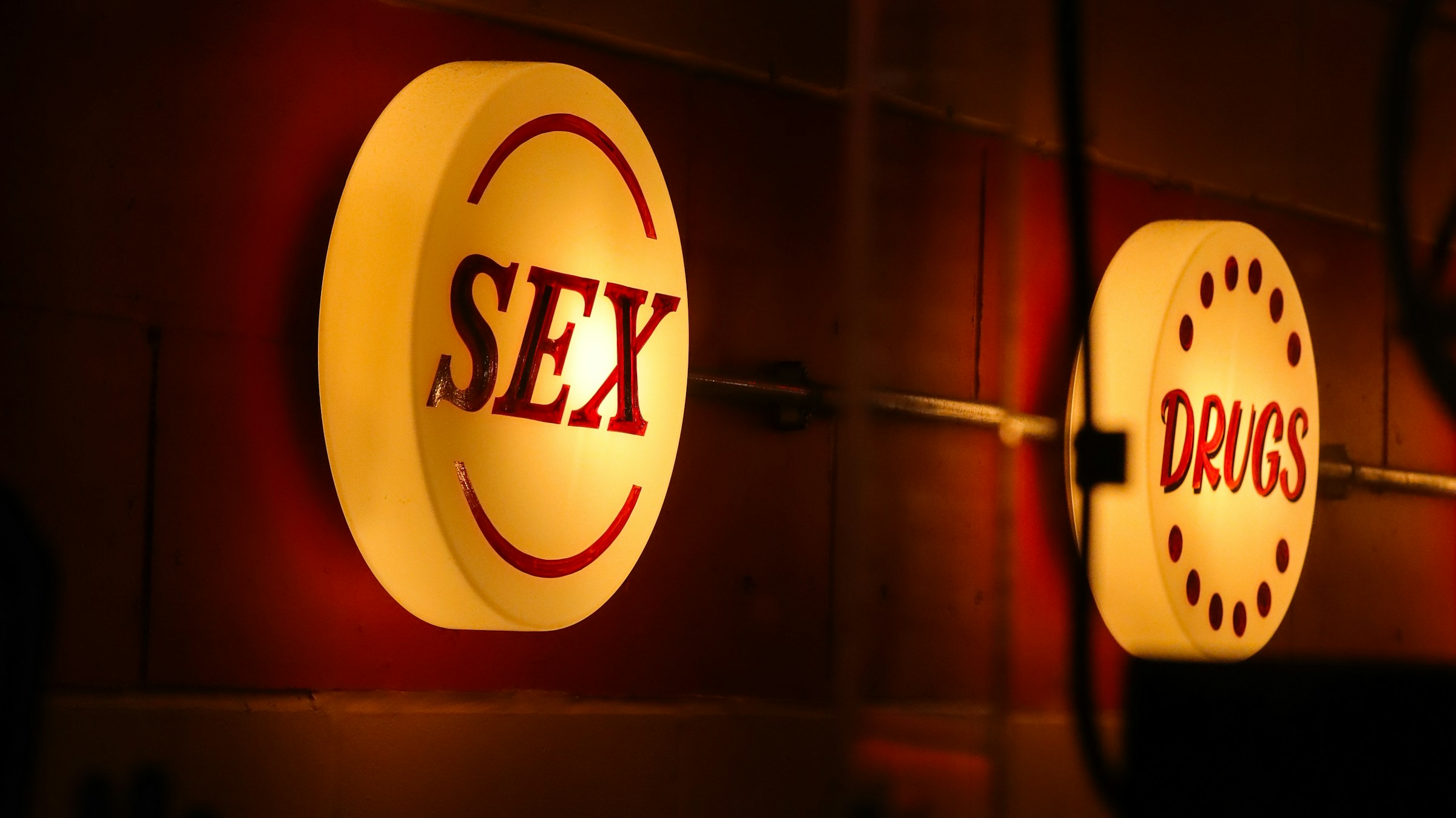 Backlit red SEX and DRUGS signs against dark tiled wall