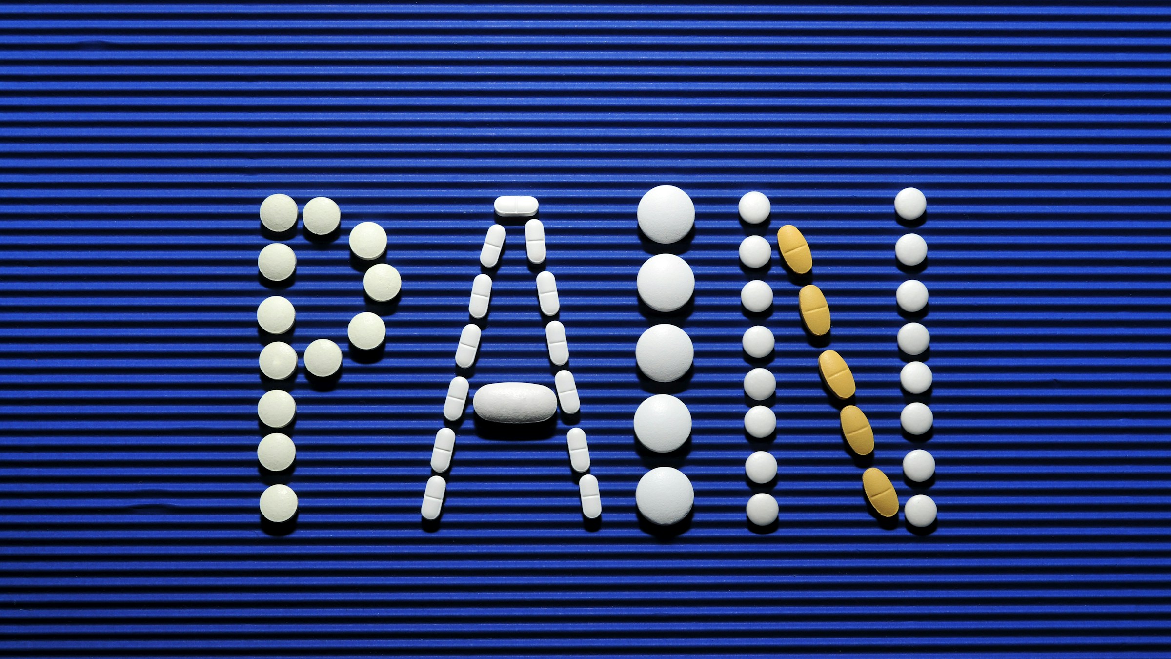 White and yellow pills arranged to spell PAIN on blue corrugated background