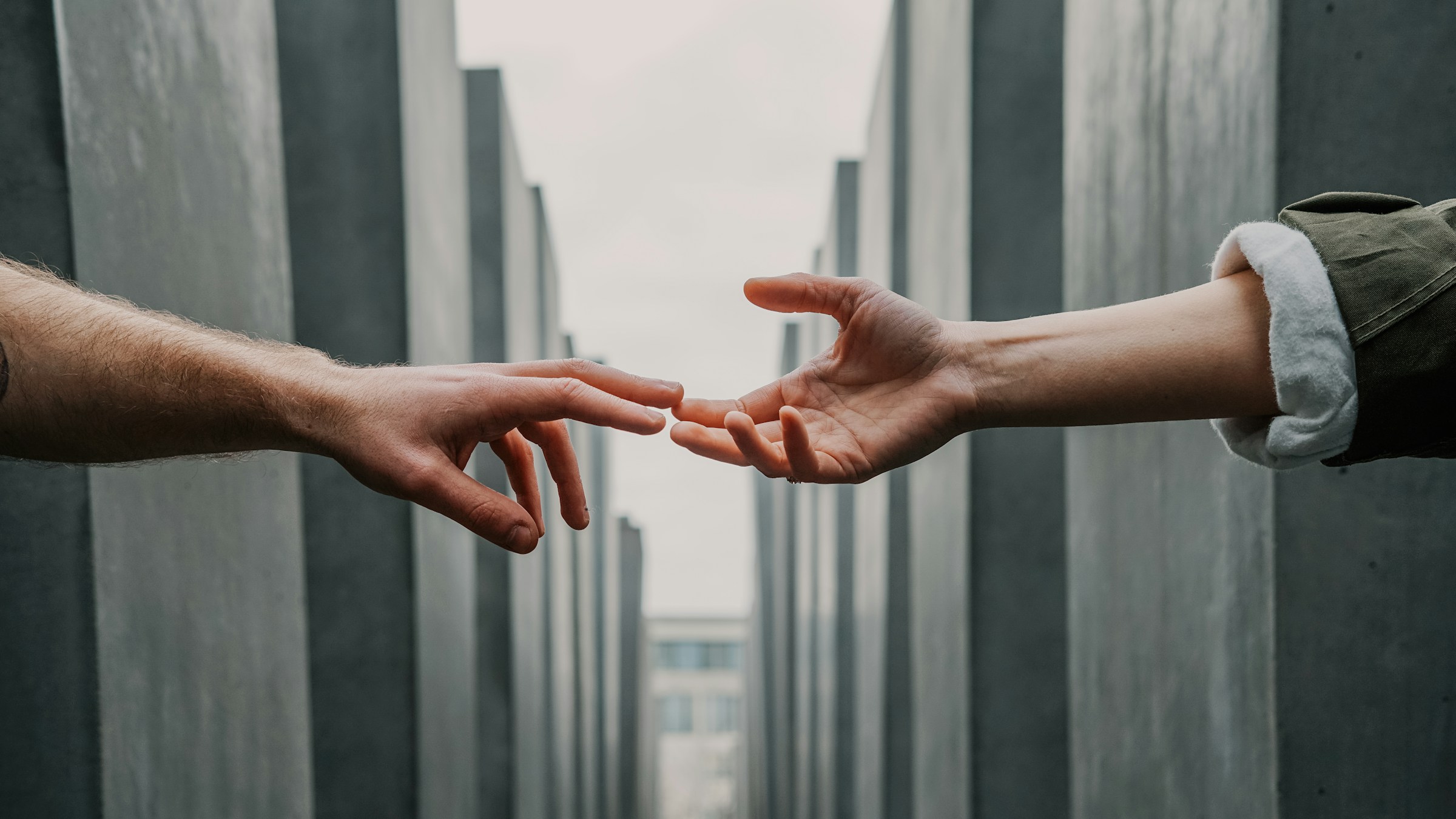 Two hands reaching toward each other between vertical concrete pillars