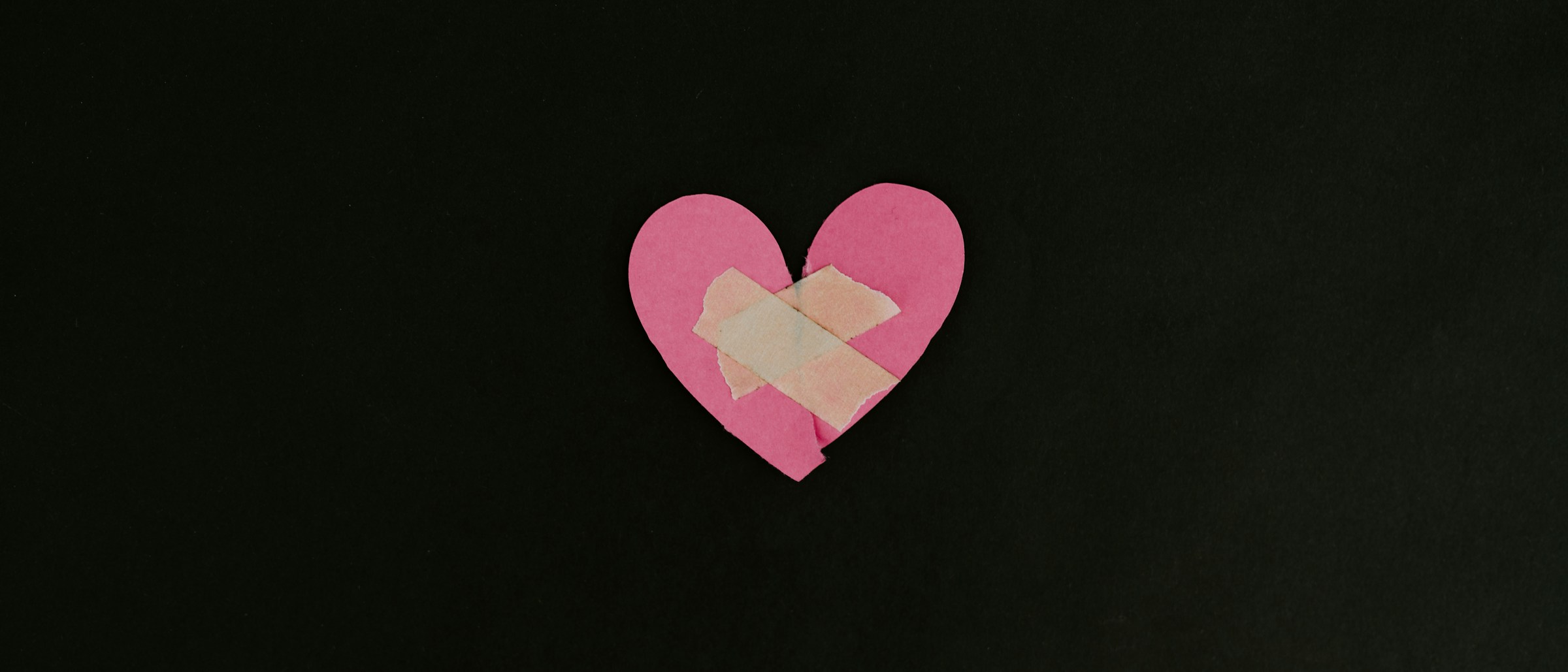 A pink paper heart with a plaster across the centre on a dark background