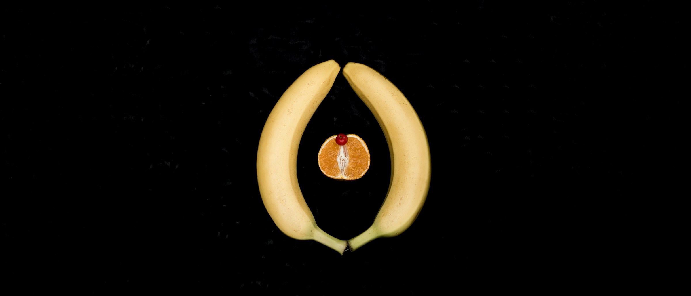 Two halved bananas and a sliced orange arranged on a black background