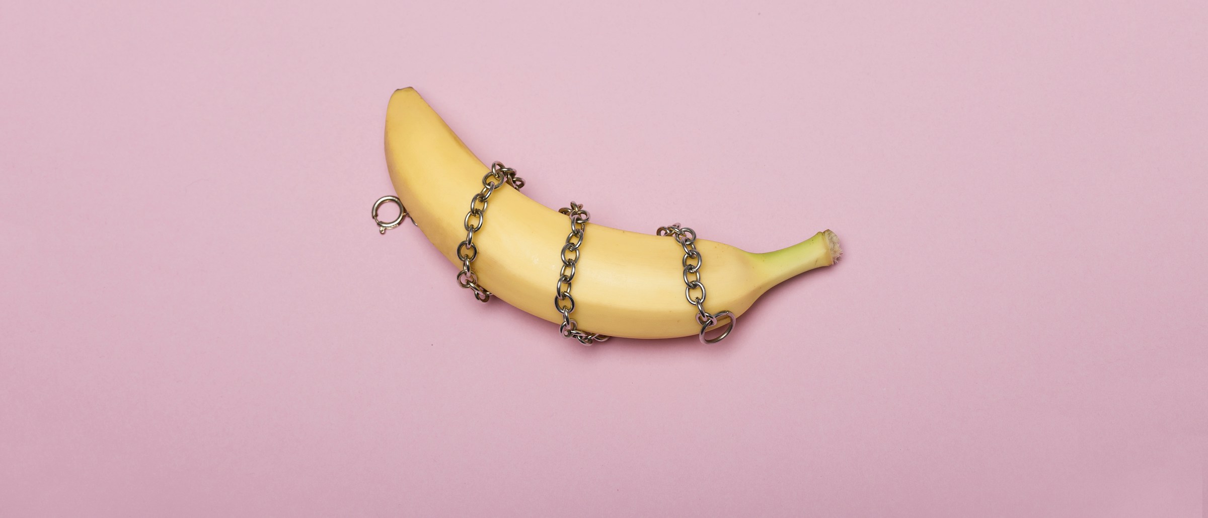 Yellow banana wearing a white condom on a teal background
