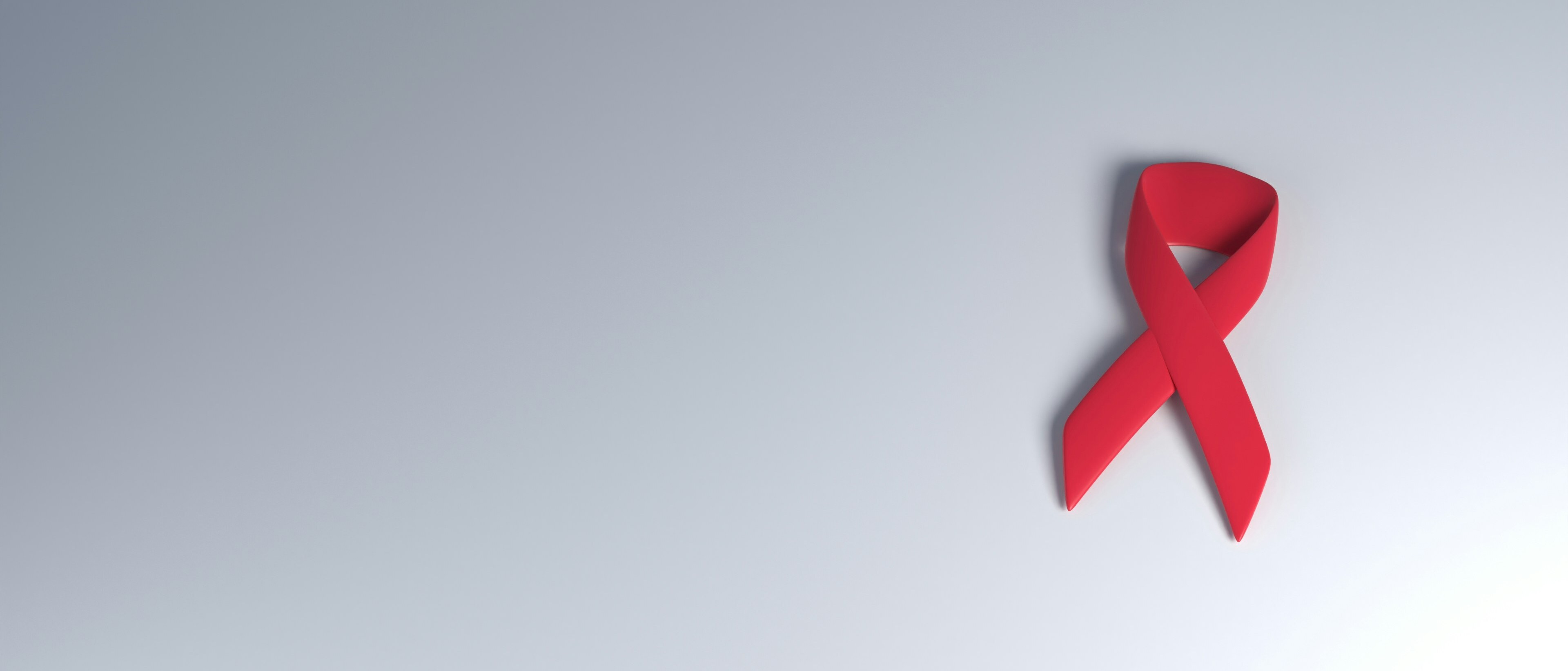 A red HIV awareness ribbon on a soft grey background
