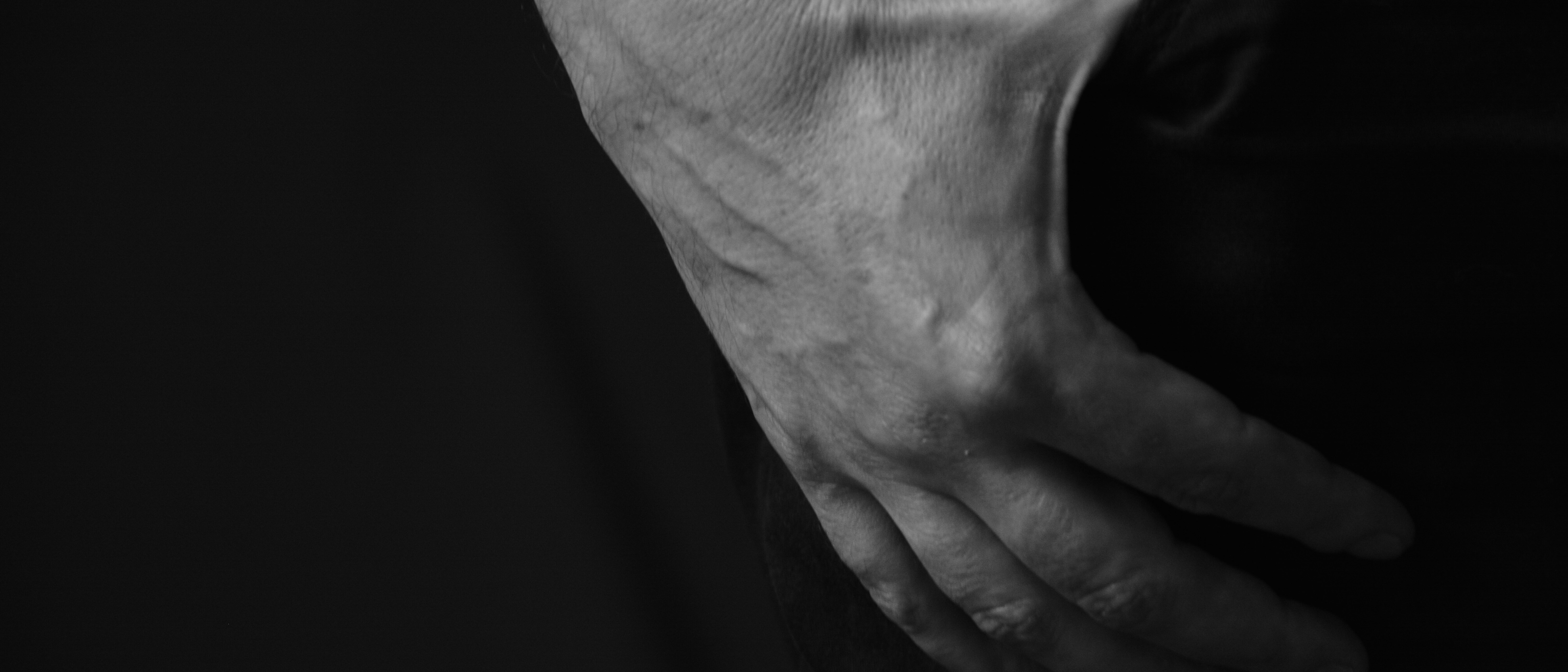 A black and white close-up of a man’s hand resting at his side