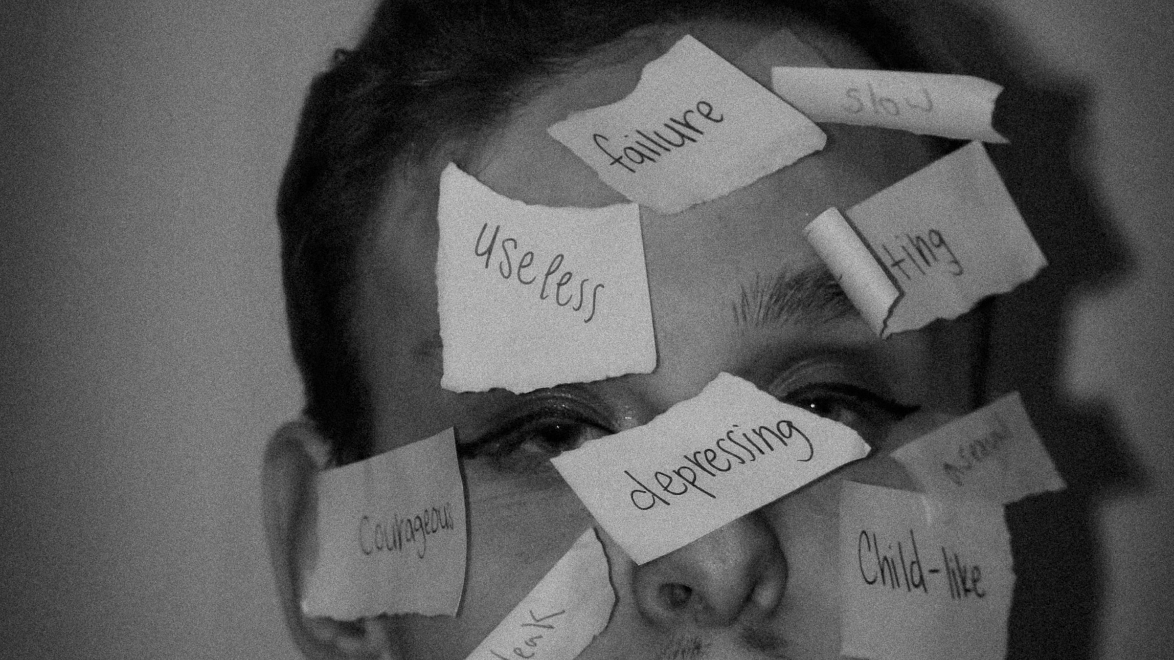 A woman’s face covered in handwritten paper labels reading failure, useless, depressing, slow, courageous, child-like
