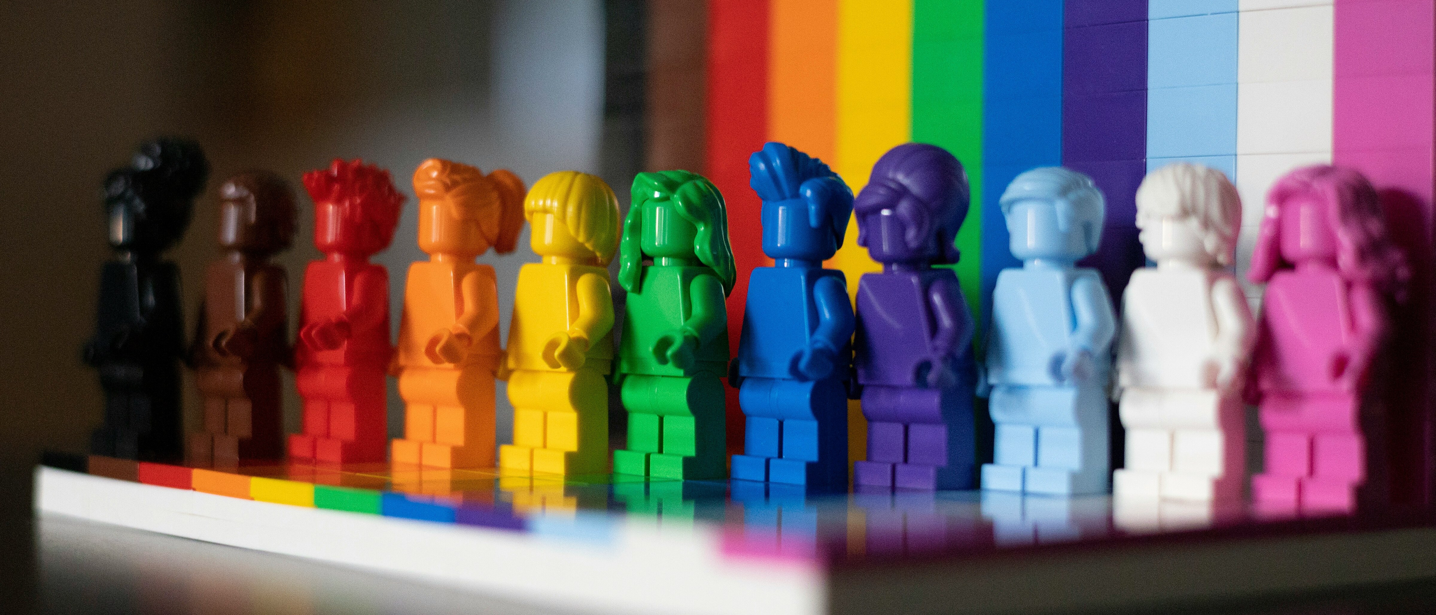 Rainbow Lego minifigures lined up in front of a brick pride flag
