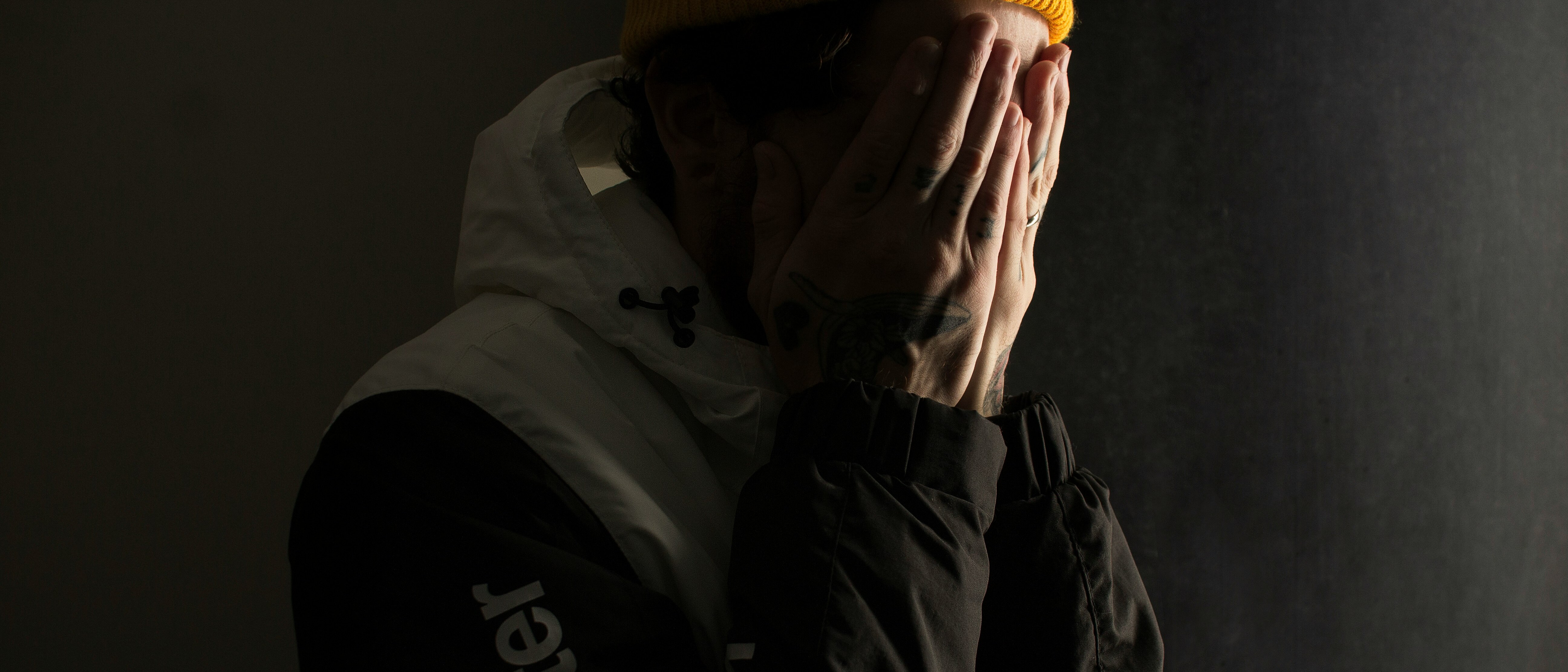 A man in a yellow beanie hiding his face in his hands